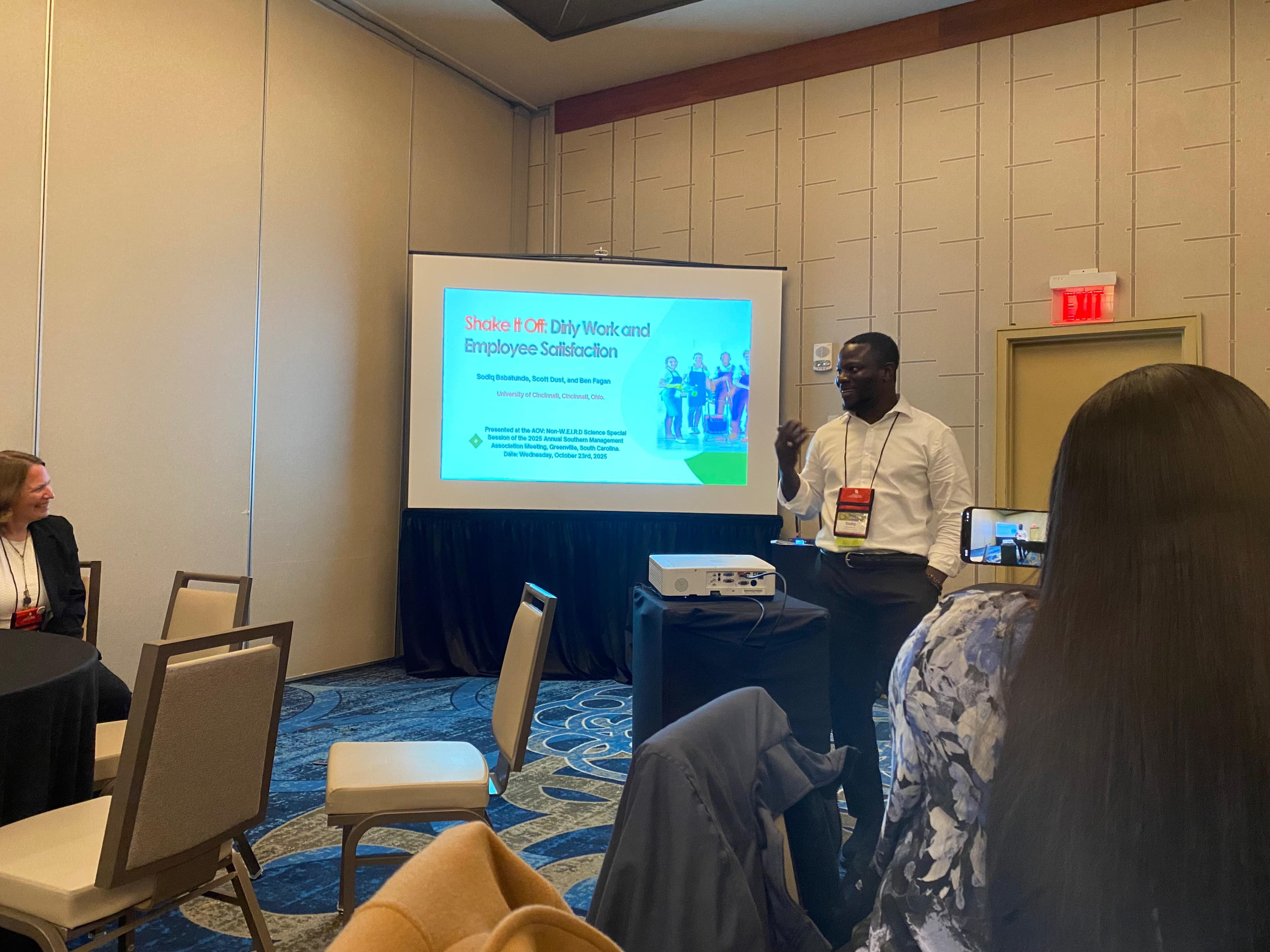 Sodiq Babatunde opening his talk “Shake It Off: Dirty Work and Employee Satisfaction” beside the title slide at the 2025 Southern Management Association meeting